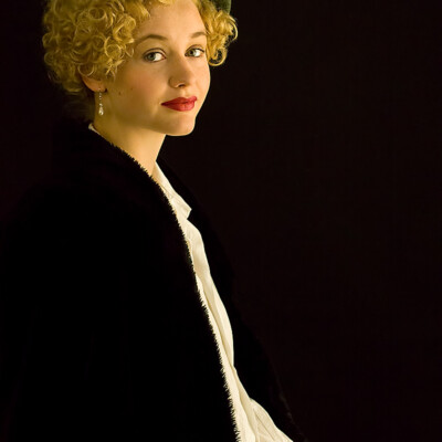 "Captivating elegance captured in the essence of the 1930s. π©β¨ Lena D. channels timeless sophistication with a touch of modern flair. #VintageStyle #MarleneInspired" "Half-close portrait of Lena D. in vintage-inspired attire against a black background, wearing a green barrett hat and brown Marlene pants."